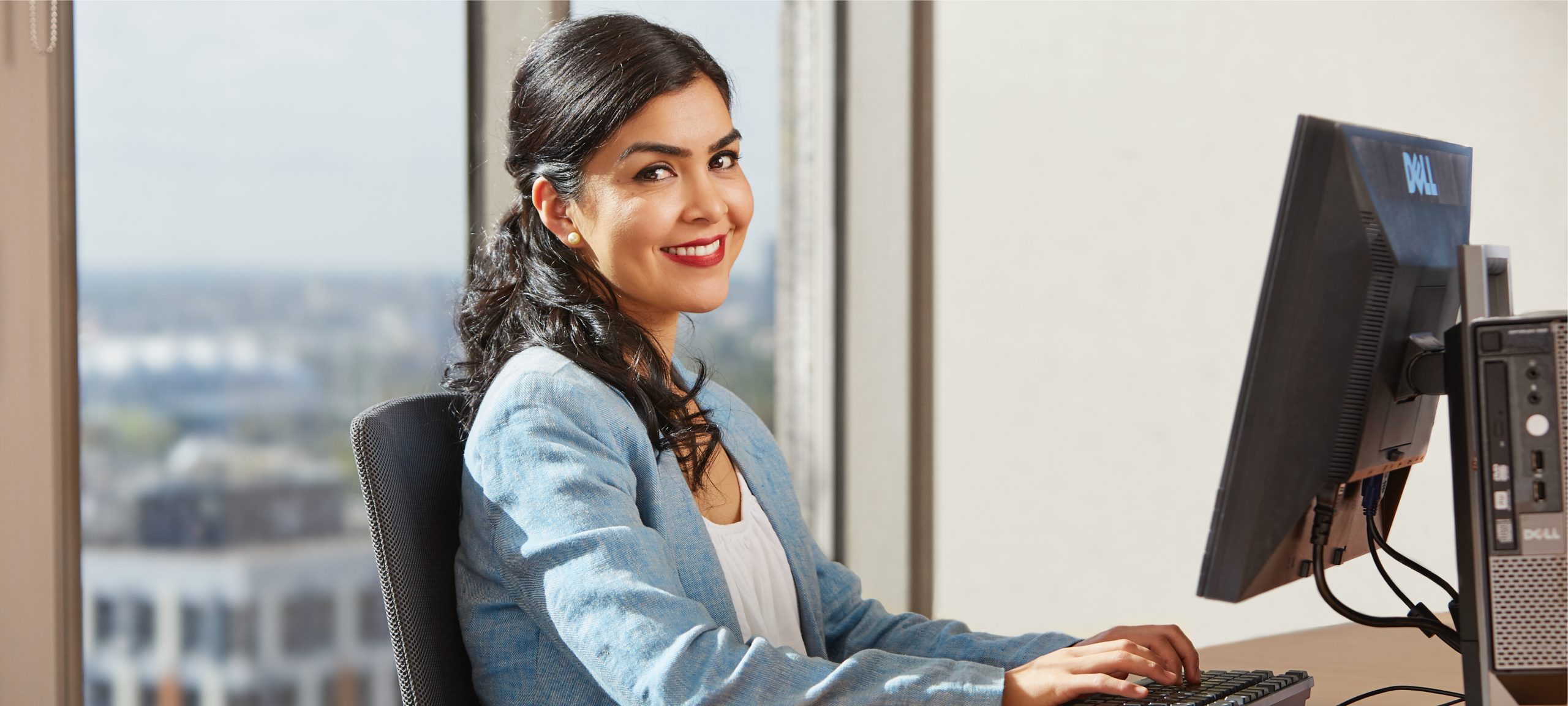 Masthead 4 A successful She Works candidate types at a computer. She is dressed professionally and smiling.