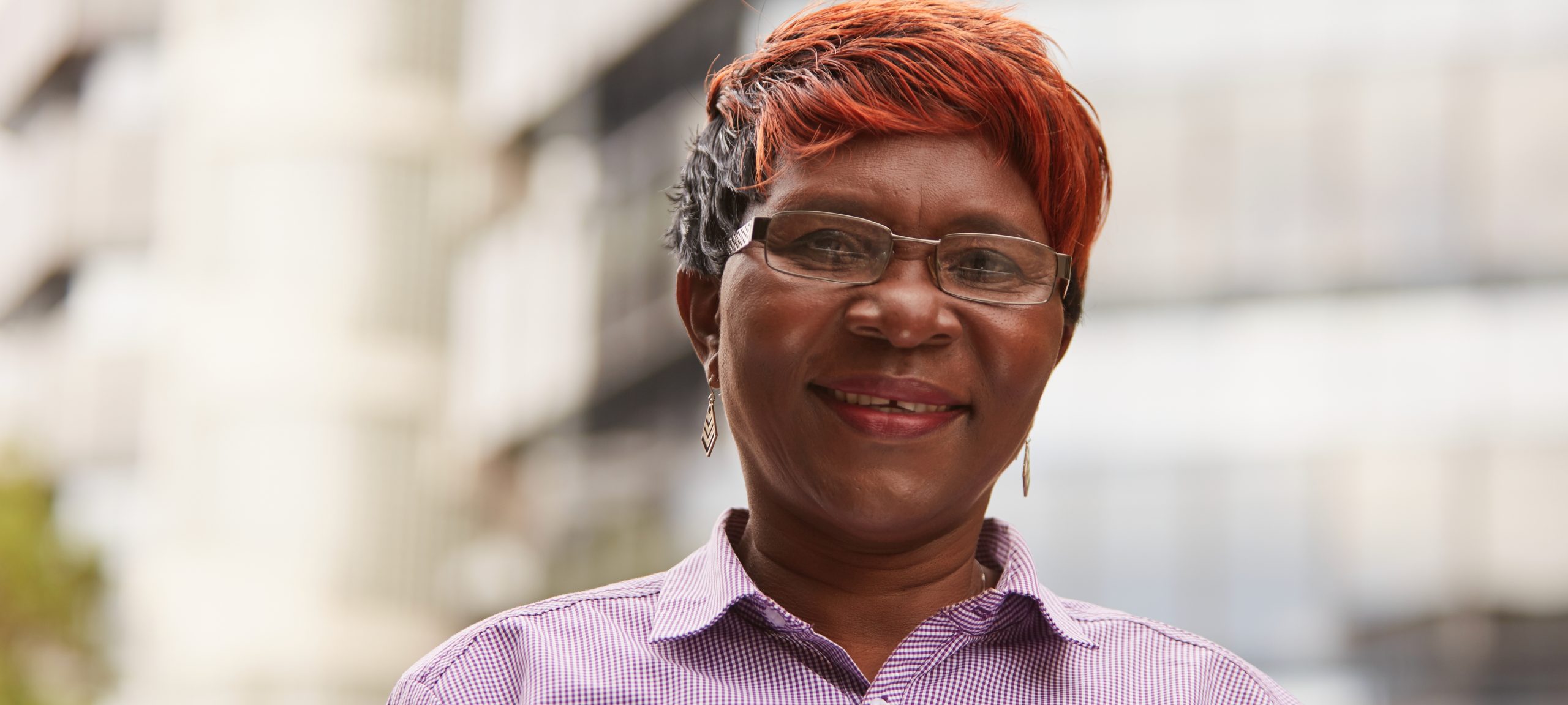 Masthead 2 A Fitted for Work client who has found work smiles. She is wearing a stylish purple shirt and glasses.