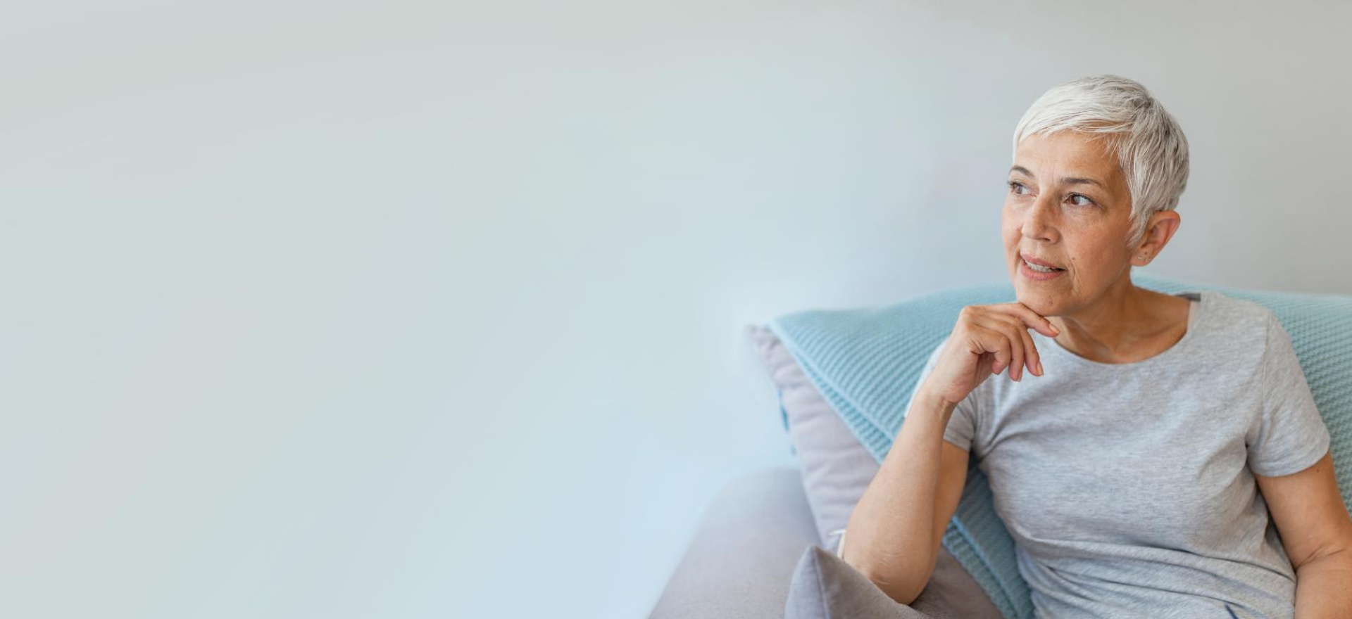 Holiday Appeal banner Esther, a Fitted for Work client is sitting on a couch. She has short white hair and is in her mid 50s. She is looking thoughtfully into the distance.