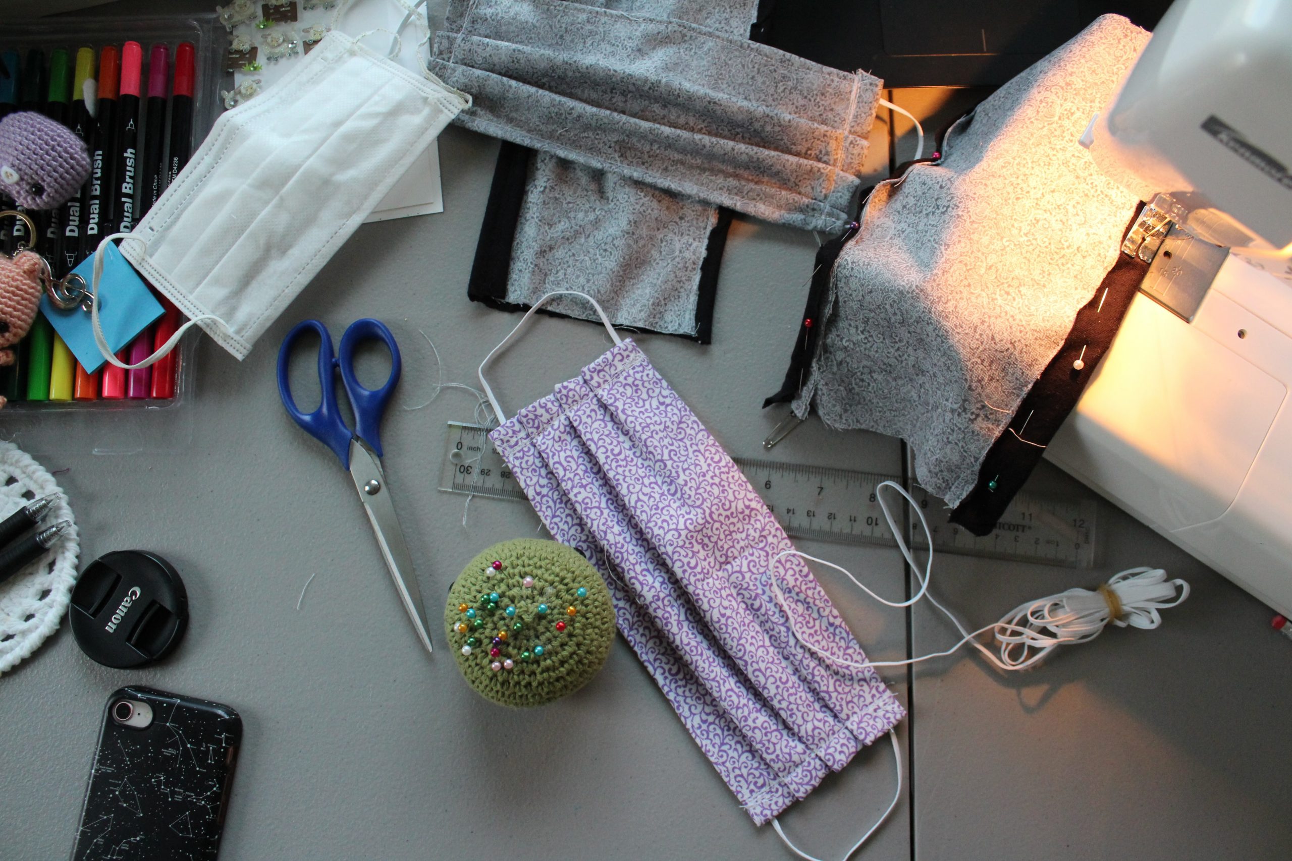 birds eye view of a desk with a sewing machine, fabric face mask, scissors and thread.
