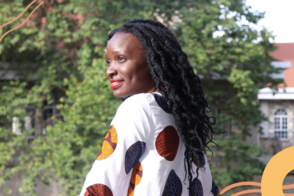 Nea wearing a white dress with a colourful pattern. She is looking into the distance and smiling.