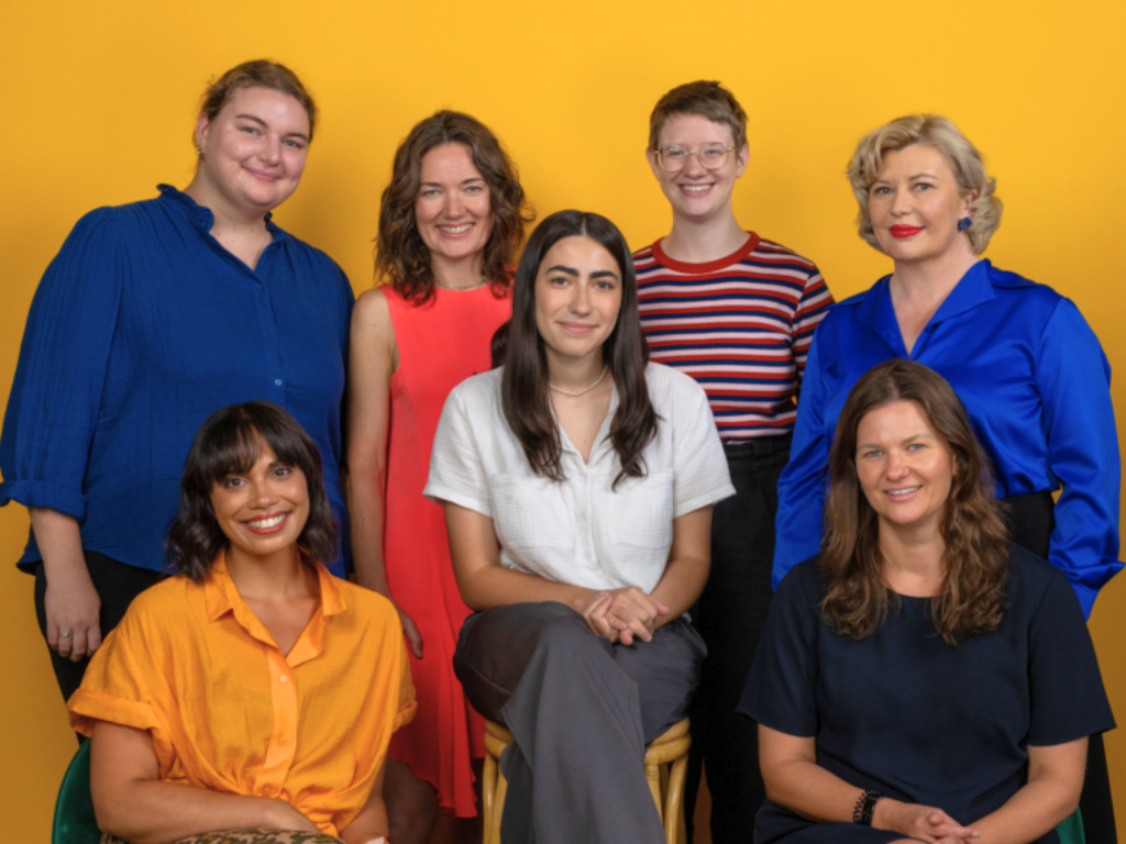 Fitted for Work team members in a group smile, with a yellow background.